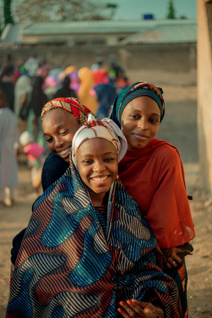 Three women in colorful attire smiling outdoors in Kaduna, Nigeria.